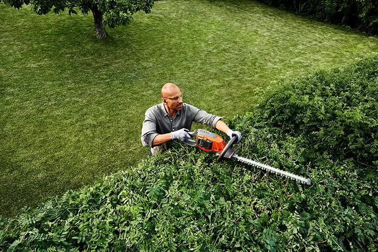 Ein Mann schneidet eine Hecke mit einer Husqvarna Heckenschere